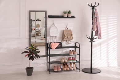 Photo of Black shelving unit with shoes and different accessories near white wall in hall. Storage idea