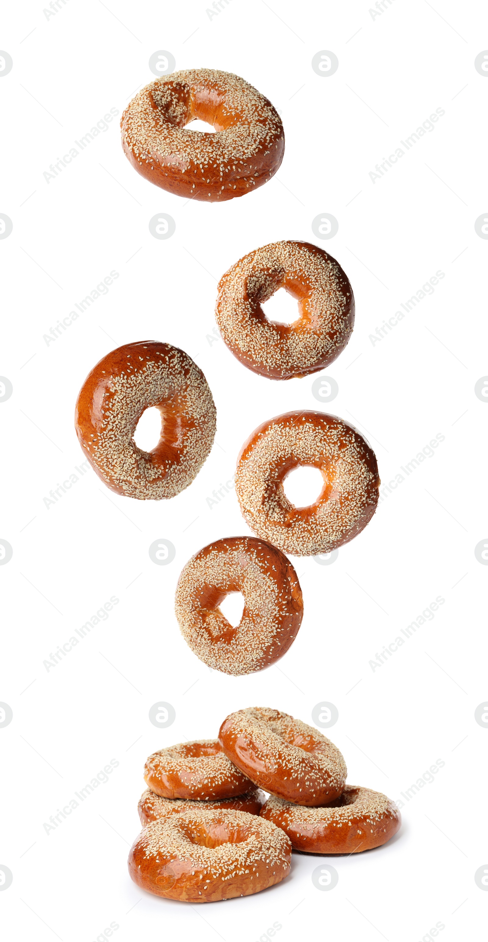 Image of Many fresh bagels with sesame seeds falling into pile on white background