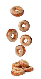 Many fresh bagels with sesame seeds falling into pile on white background