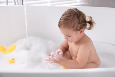 Photo of Cute little girl taking bubble bath with toys indoors