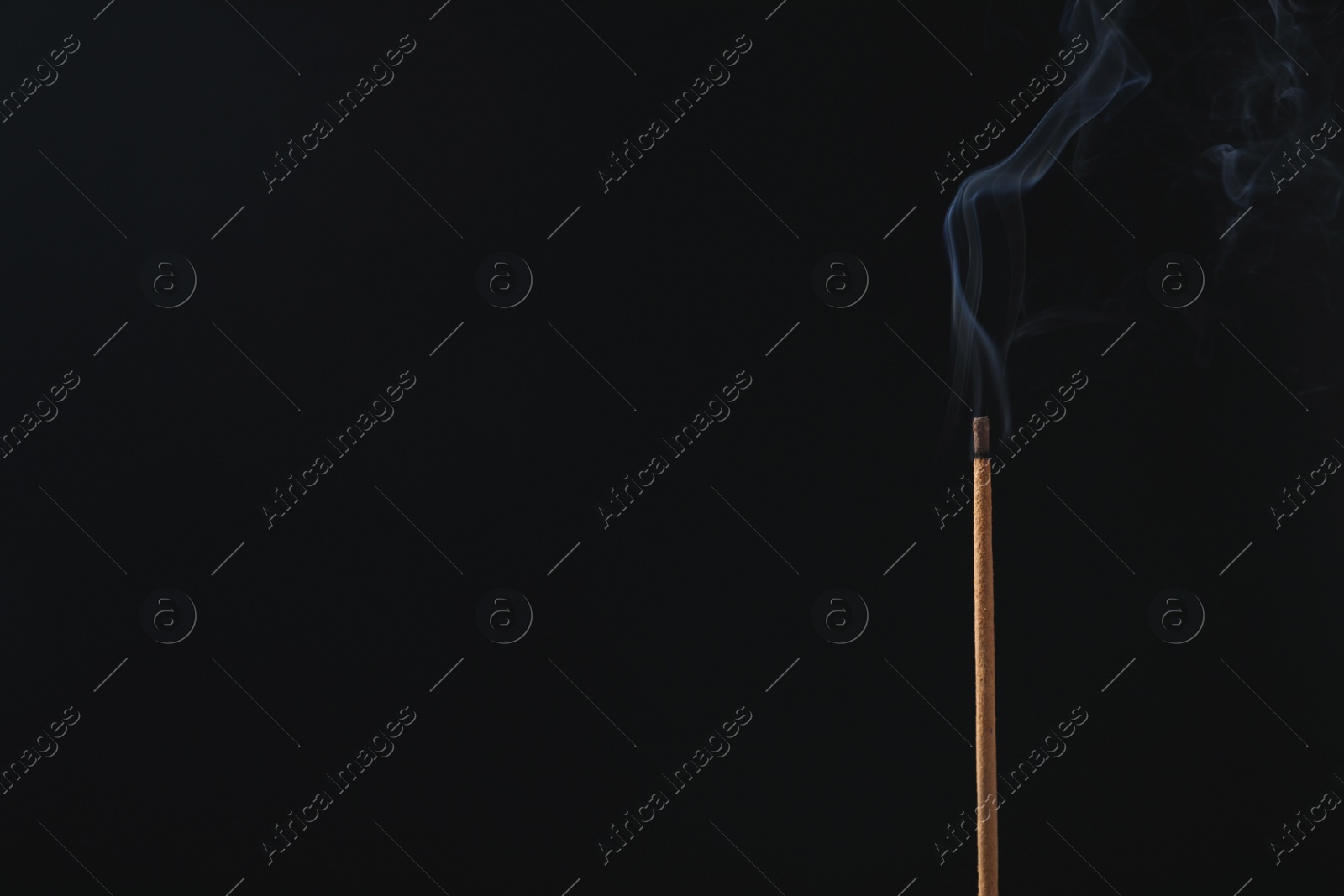 Photo of Incense stick smoldering on black background. Space for text