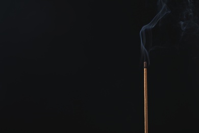 Photo of Incense stick smoldering on black background. Space for text