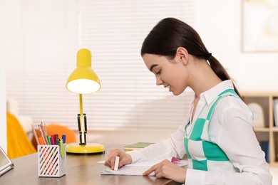 Photo of Teenage girl erasing mistake in her notebook at wooden desk indoors