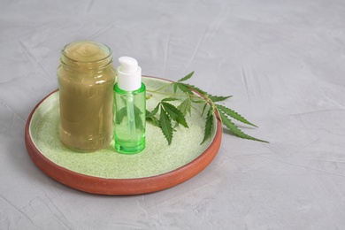 Photo of Tray with containers of hemp lotion and oil on gray table. Space for text