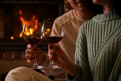 Lovely couple with glasses of wine near fireplace indoors, closeup. Winter vacation