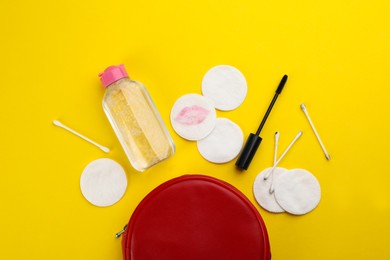 Photo of Dirty cotton pads, swabs, mascara and micellar cleansing water on yellow background, flat lay