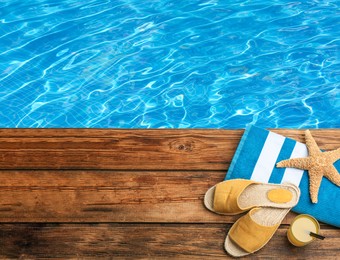 Image of Beach accessories and juice on wooden on wooden surface near swimming pool, above view. Space for text