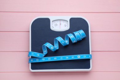 Bathroom scale and measuring tape on pink wooden floor, top view. Weight loss concept