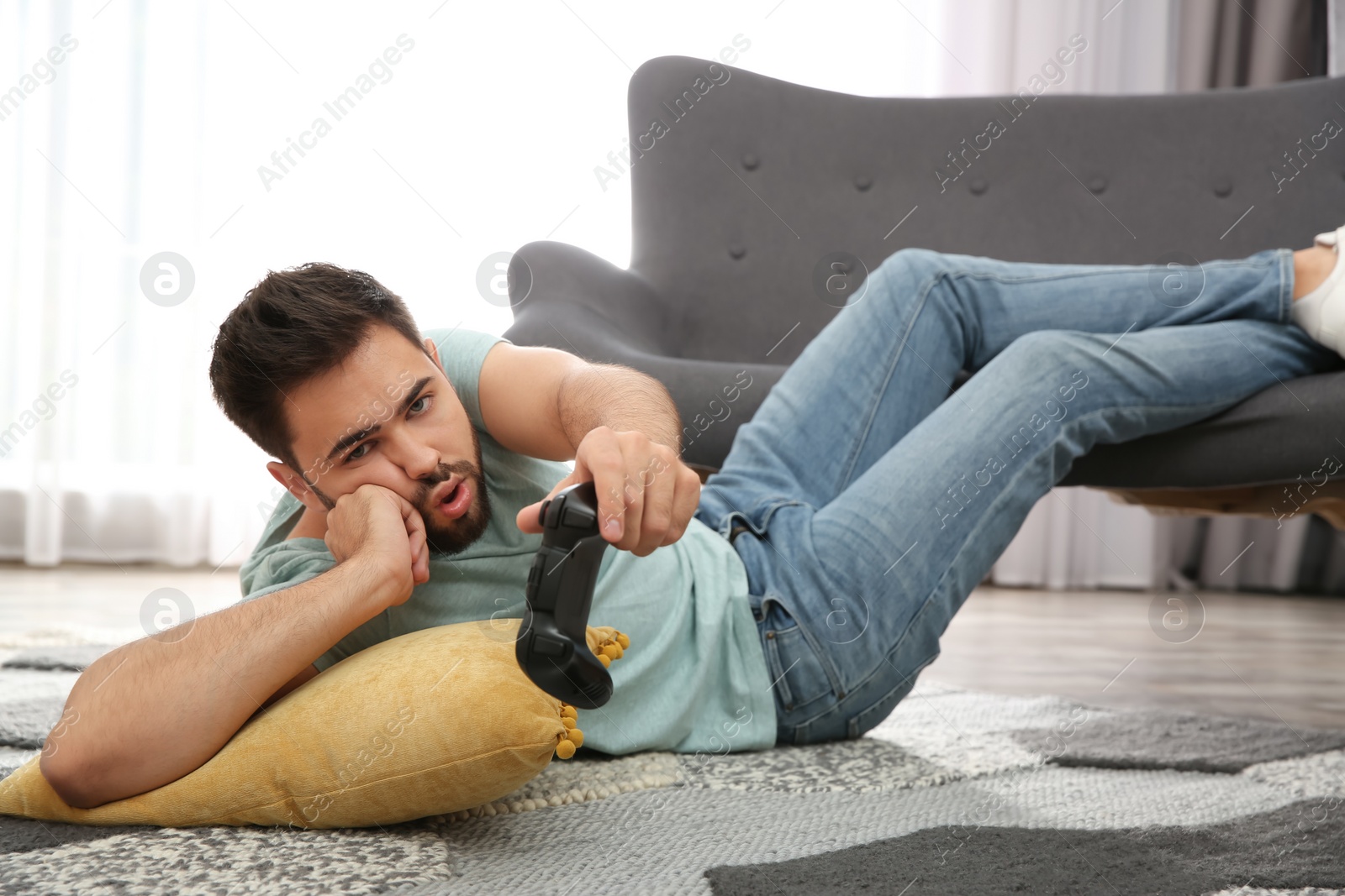 Photo of Lazy young man playing video game while lying on floor at home