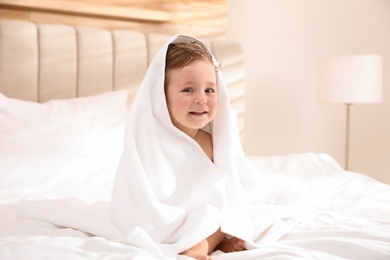 Cute little baby with soft towel on bed after bath