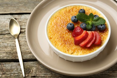 Photo of Delicious creme brulee with berries and mint in bowl on wooden table, closeup