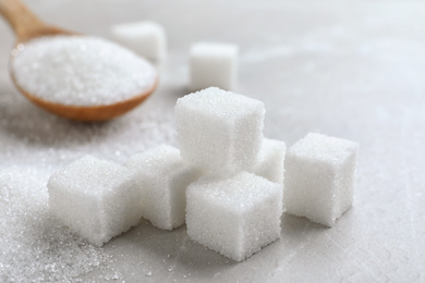 Photo of Heap of refined sugar cubes on light grey table, closeup