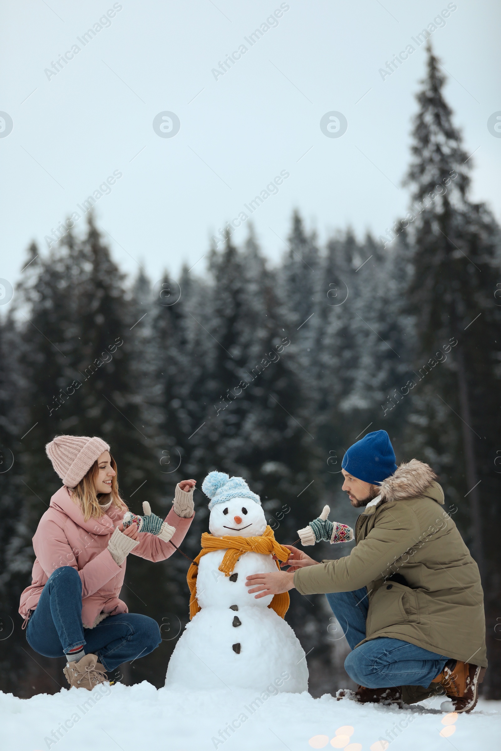 Photo of Couple making snowman near forest, space for text. Winter vacation