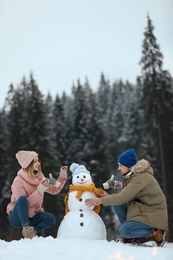 Photo of Couple making snowman near forest, space for text. Winter vacation