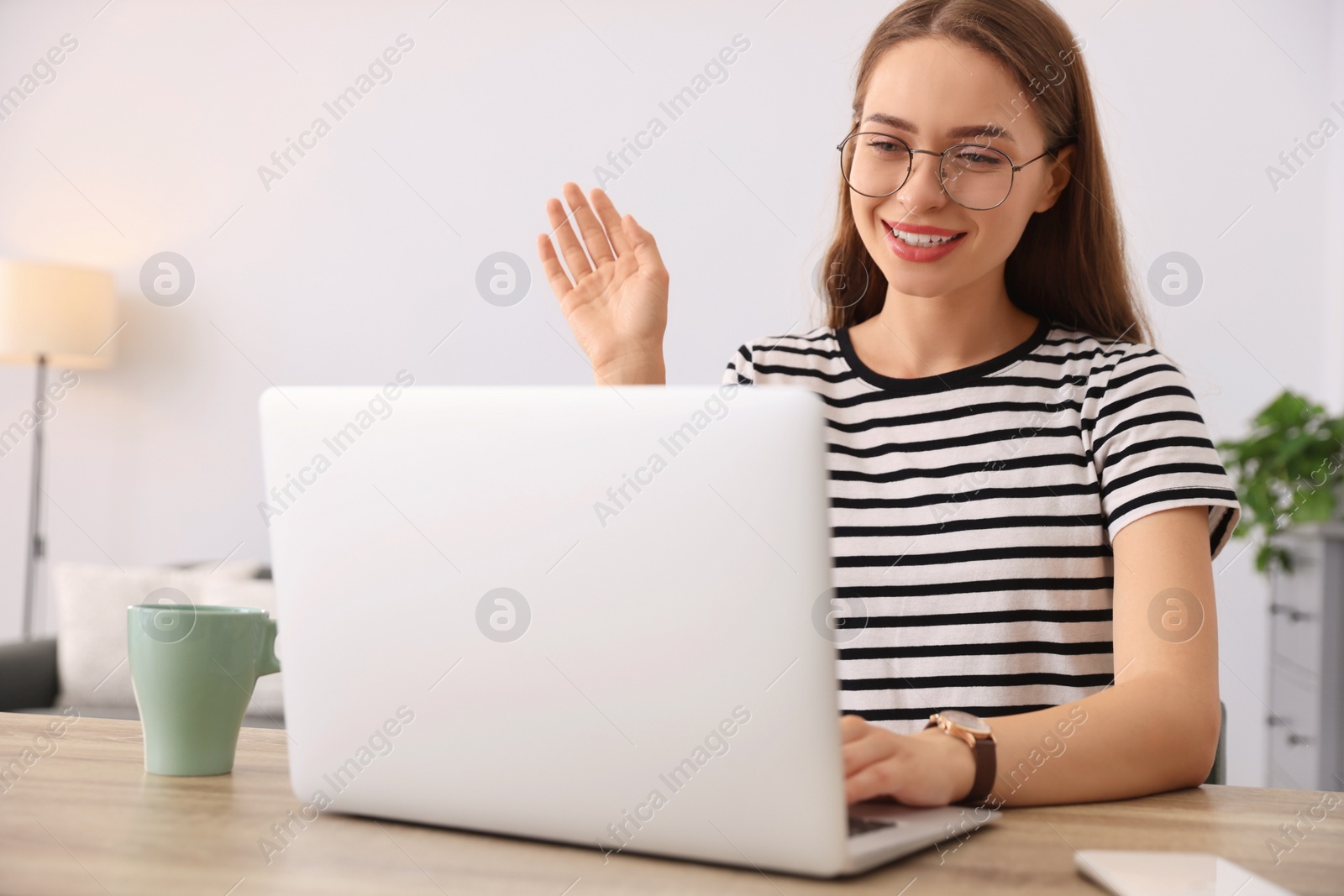 Photo of Happy young woman having video chat on laptop at table indoors