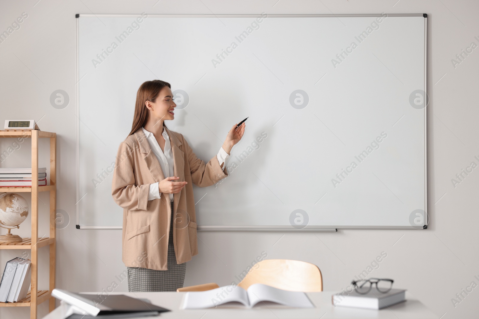 Photo of Happy young teacher explaining something at whiteboard in classroom. Space for text