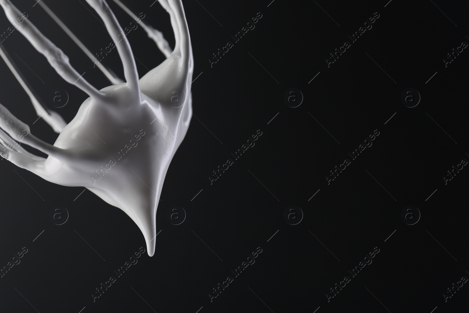 Photo of Whisk with whipped cream on black background, closeup. Space for text