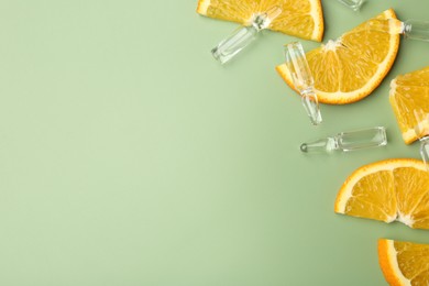 Skincare ampoules with vitamin C, slices of orange and leaves on light green background, flat lay. Space for text