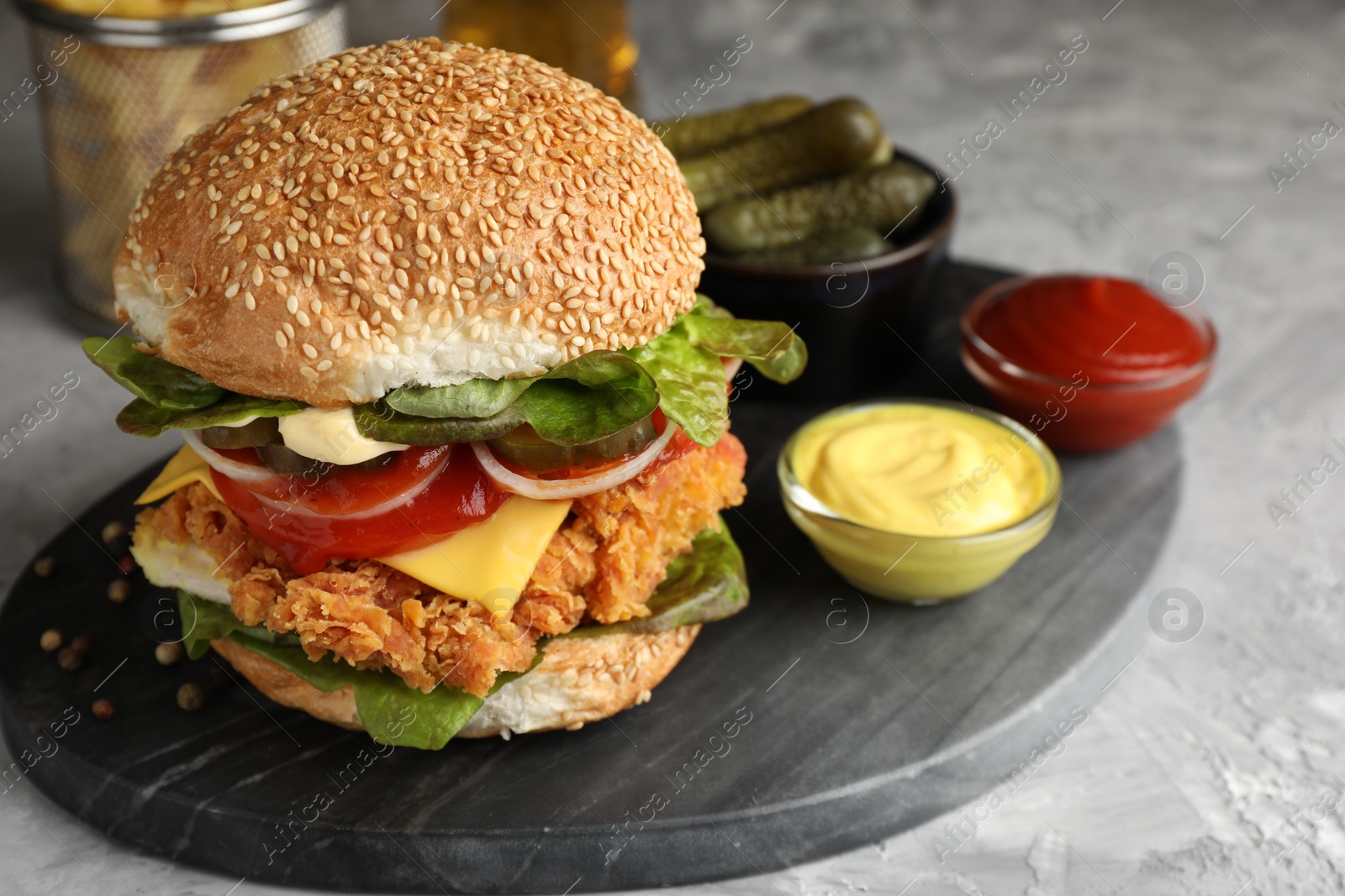 Photo of Delicious burger with crispy chicken patty and sauces on grey table, closeup