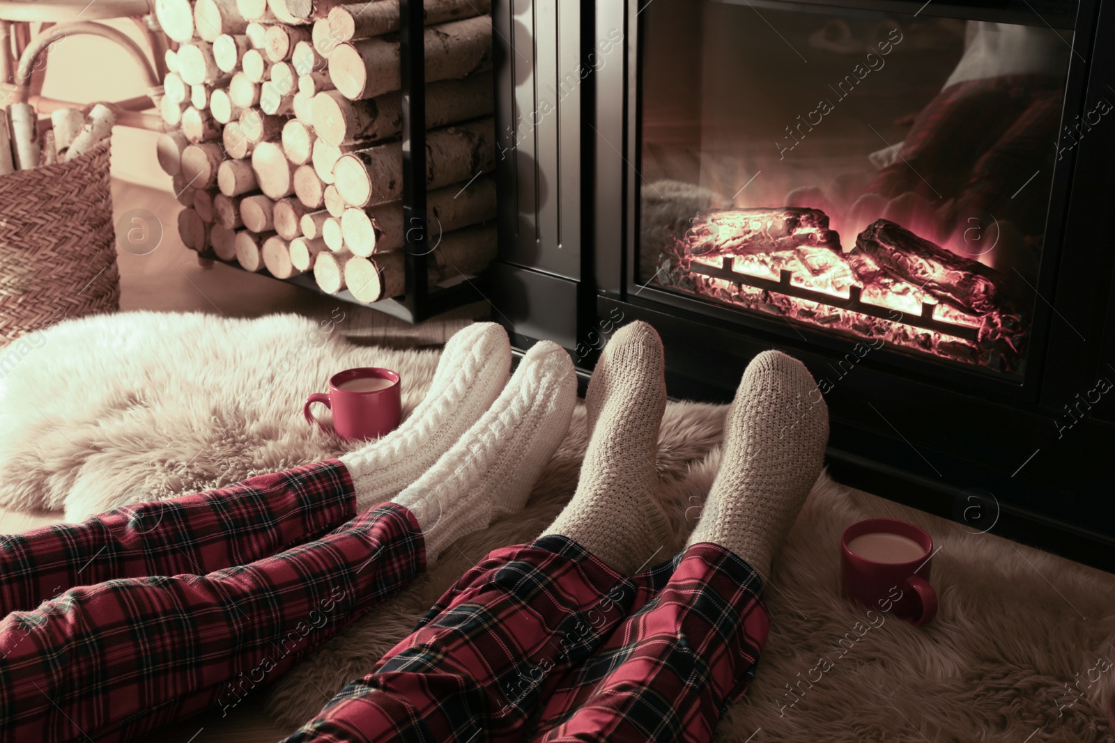 Photo of Couple in knitted socks near fireplace at home, closeup of legs