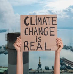 Image of Protestor holding placard with text Climate Change Is Real  and blurred view of industrial factory on background 