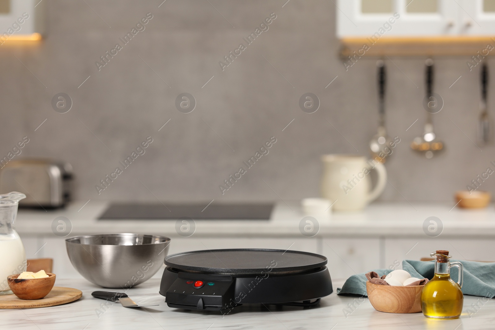 Photo of Electrical crepe maker and ingredients on white marble table in kitchen, space for text