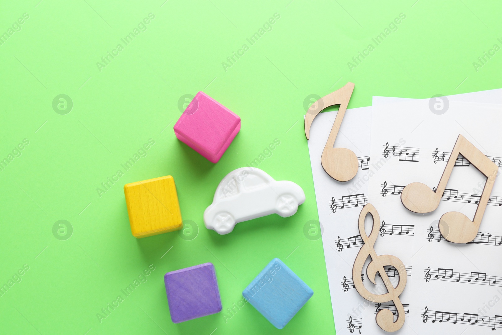 Photo of Wooden notes, music sheets and toys on light green background, flat lay with space for text. Baby song concept