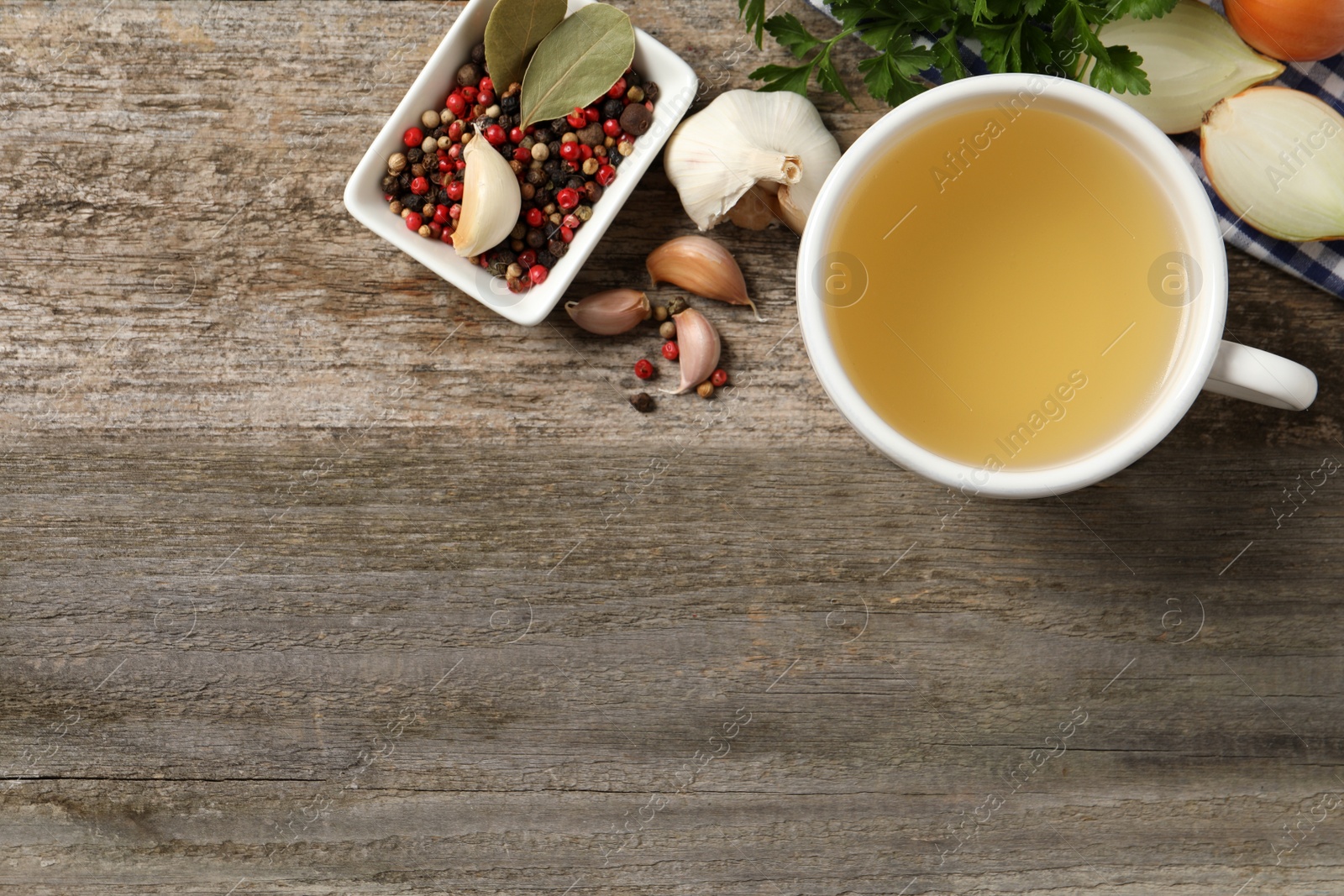 Photo of Hot delicious bouillon in cup and ingredients on wooden table, flat lay. Space for text