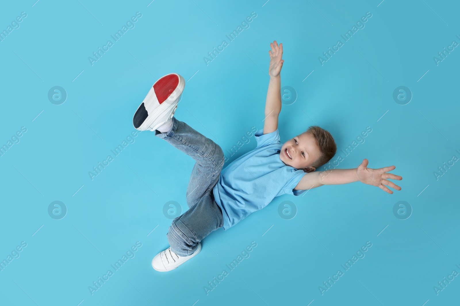 Photo of Happy little boy dancing on light blue background, top view