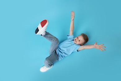 Happy little boy dancing on light blue background, top view