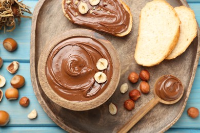 Photo of Flat lay composition with tasty chocolate paste and hazelnuts on light blue wooden table