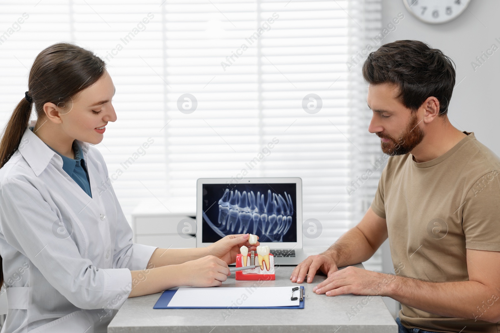 Photo of Doctor showing patient educational model of dental implant in clinic