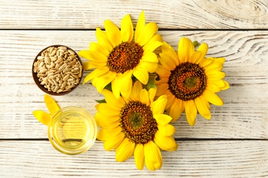 Photo of Sunflowers, oil and seeds on white wooden table, flat lay