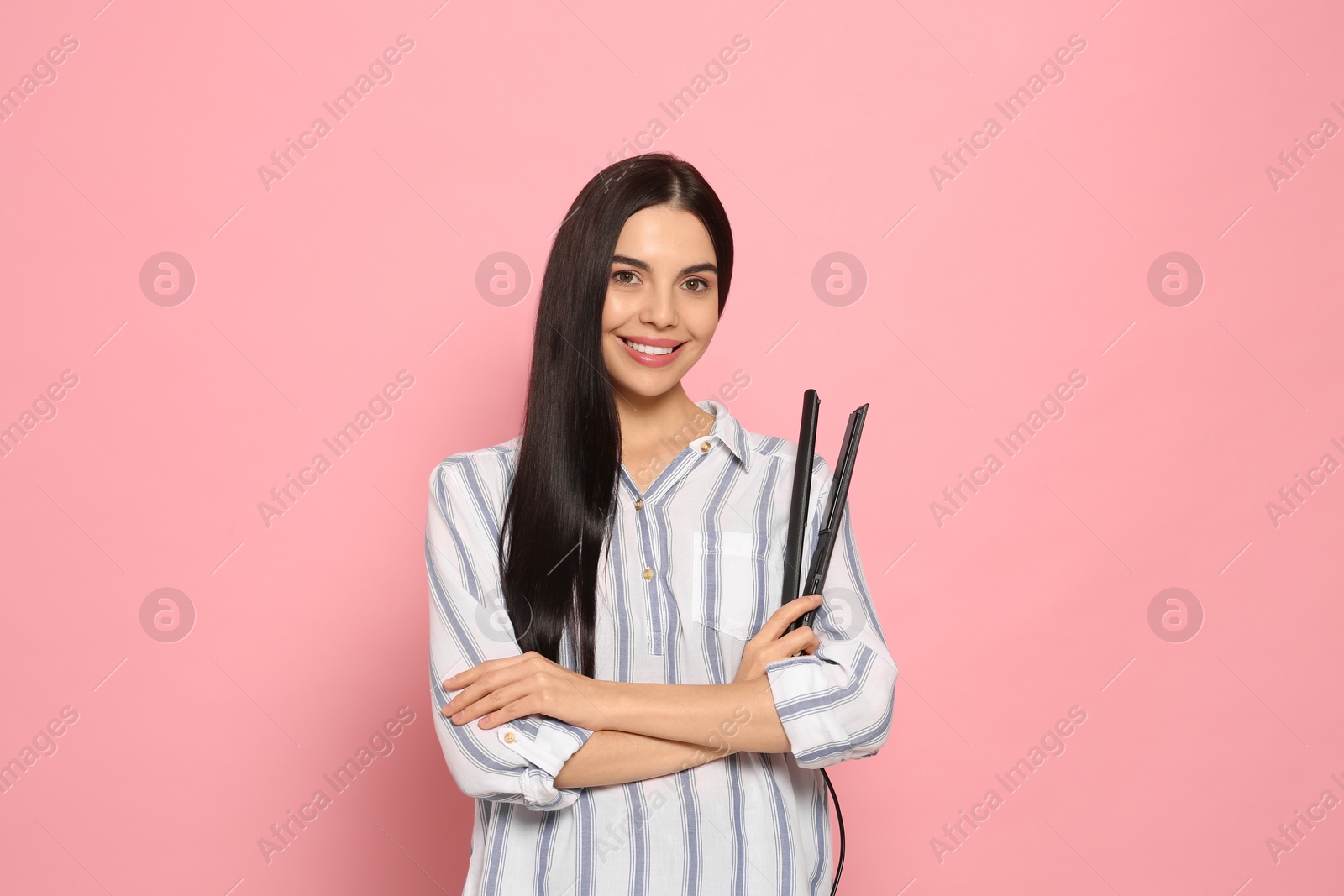 Photo of Beautiful happy woman with hair iron on pink background