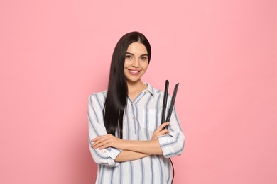Beautiful happy woman with hair iron on pink background