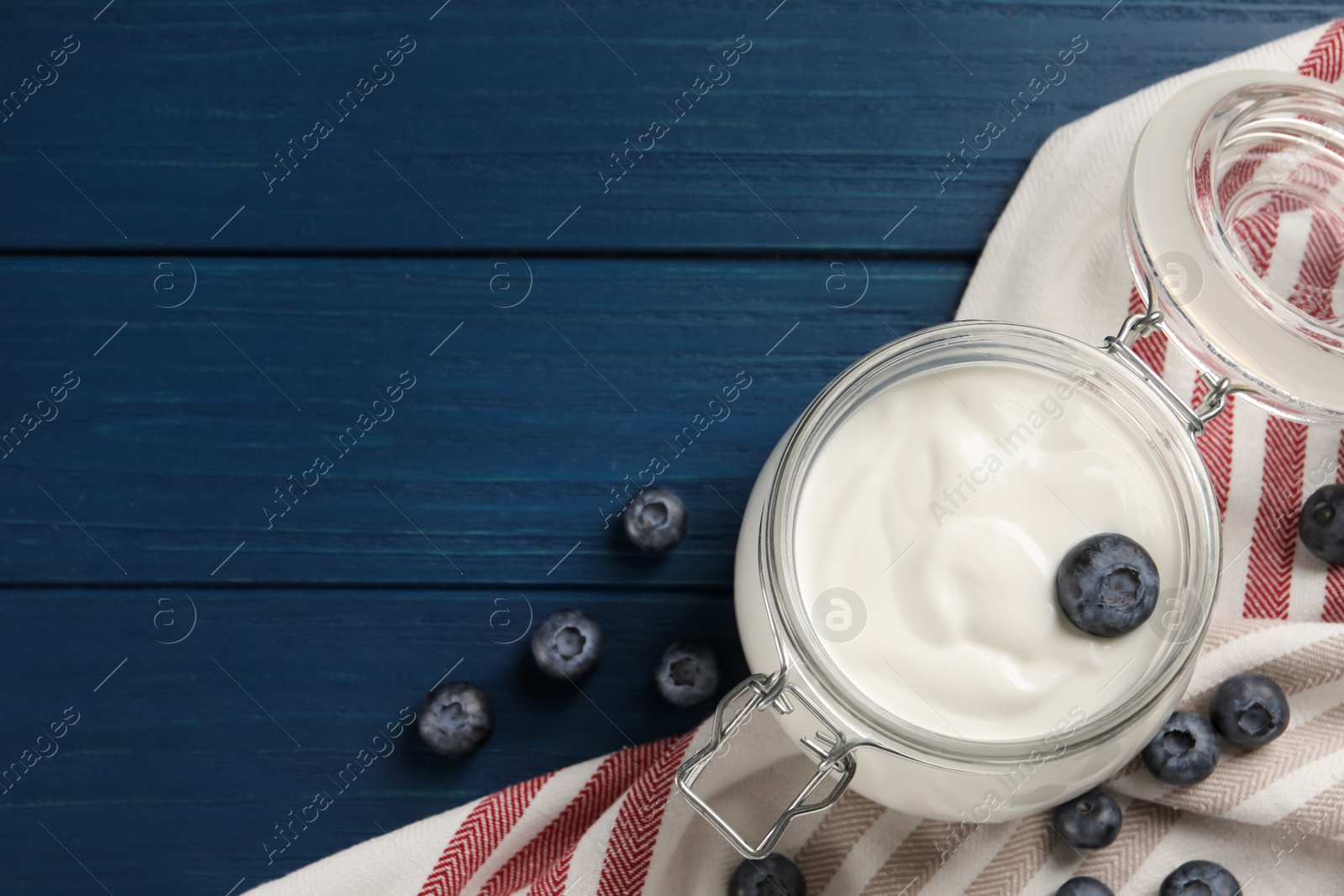 Photo of Jar of tasty yogurt served with blueberries on blue wooden table, flat lay. Space for text