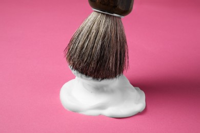 Photo of Dipping brush into shaving foam on pink background, closeup