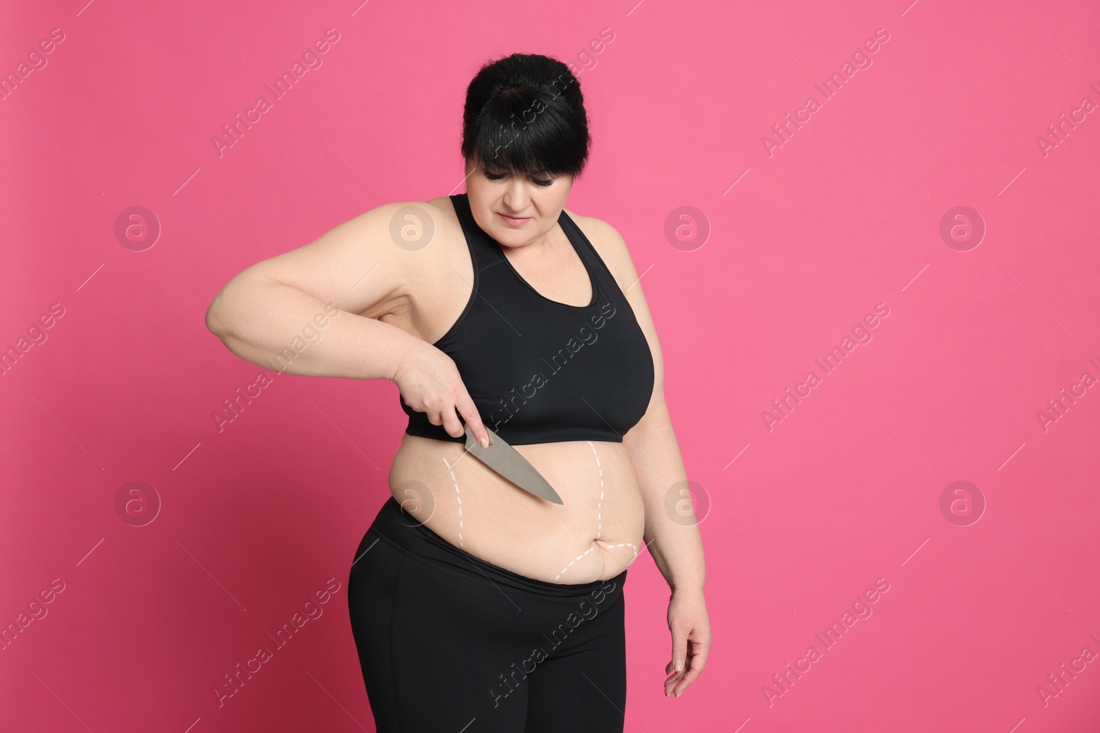 Photo of Obese woman with knife and marks on body against pink background. Weight loss surgery