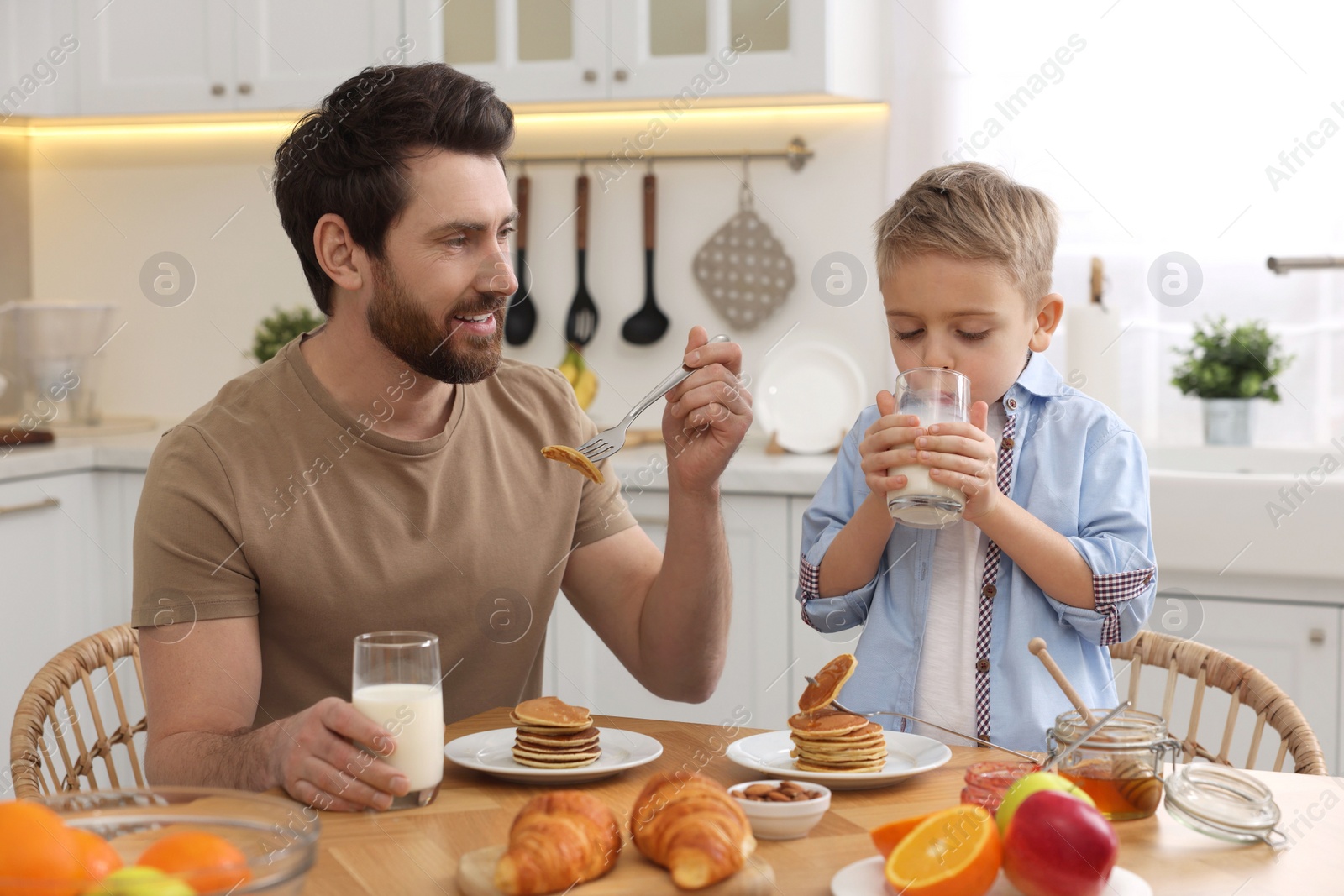 Photo of Father and his cute little son having breakfast at table in kitchen