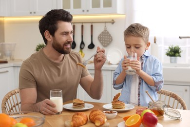 Father and his cute little son having breakfast at table in kitchen