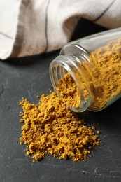 Photo of Jar with dry curry powder on dark textured table, closeup