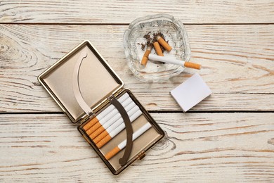 Photo of Cigarettes in case, matchbox and ashtray with stubs on white wooden table, flat lay