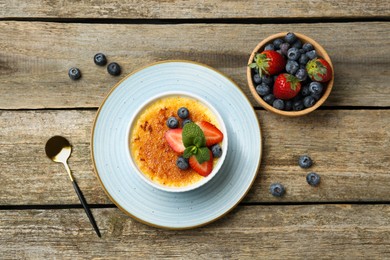 Delicious creme brulee with berries and mint in bowl served on wooden table, flat lay