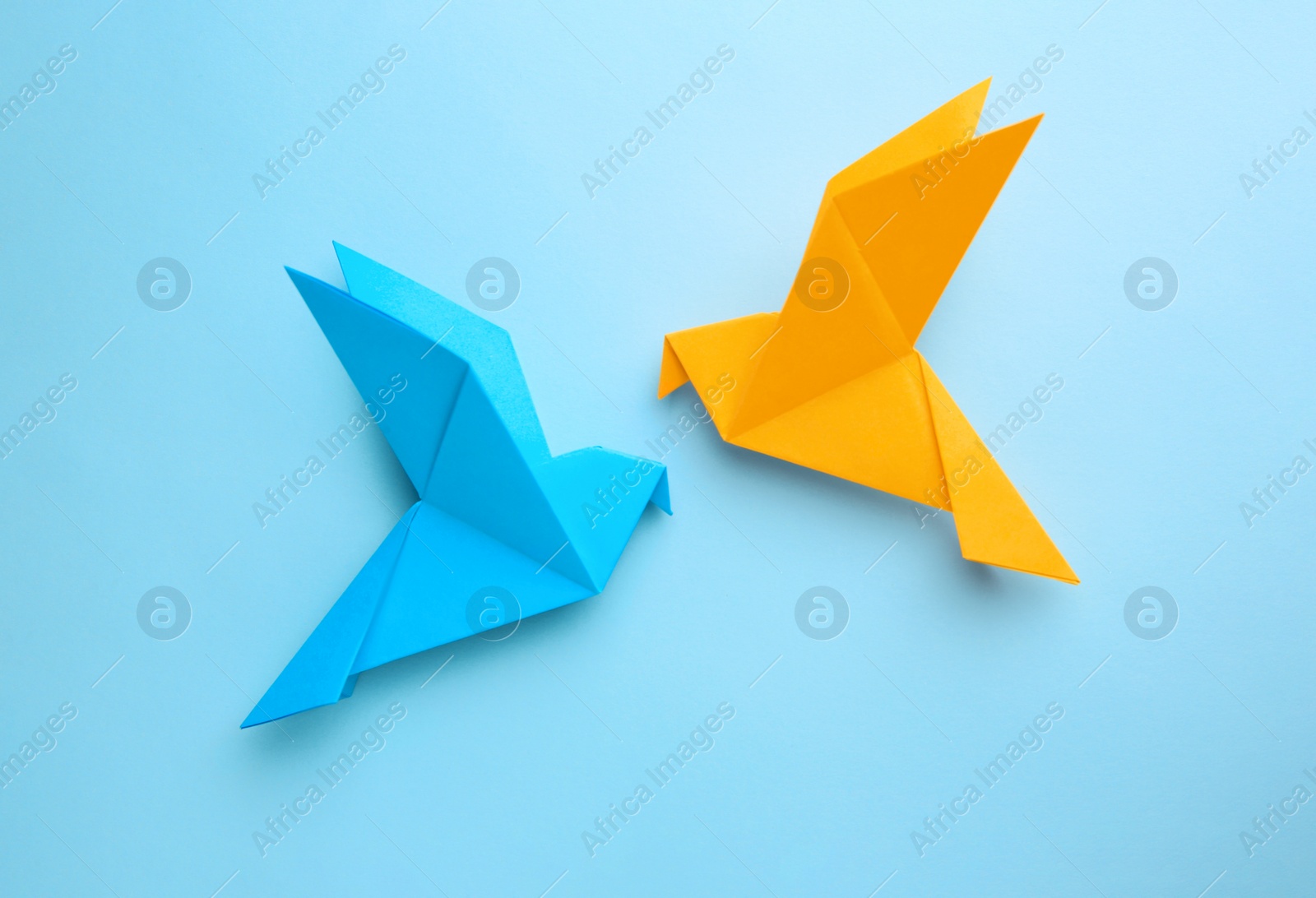 Photo of Origami art. Colorful handmade paper birds on light blue background, flat lay