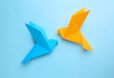 Photo of Origami art. Colorful handmade paper birds on light blue background, flat lay