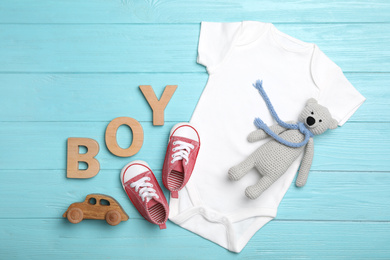 Photo of Flat lay composition with child's clothes, booties and word Boy on light blue background