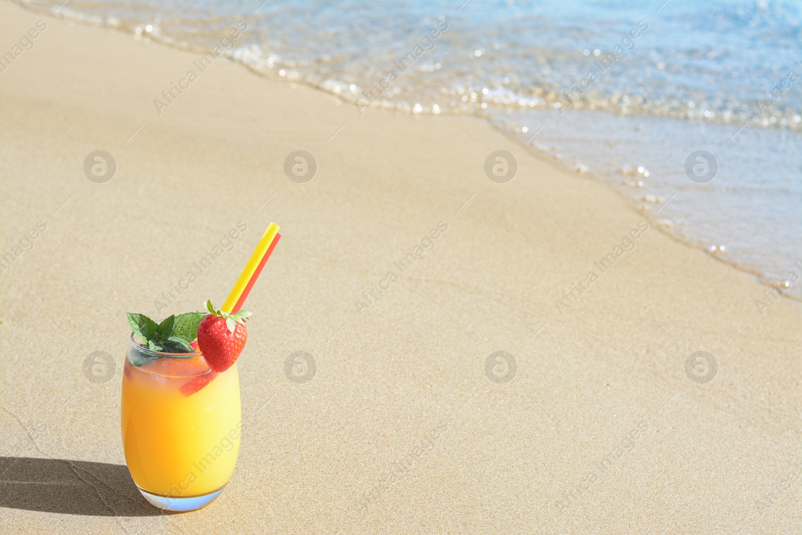 Photo of Glass of refreshing drink with strawberry on sandy beach near sea, space for text