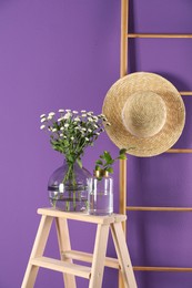 Stylish vase with chrysanthemum bouquet near purple wall