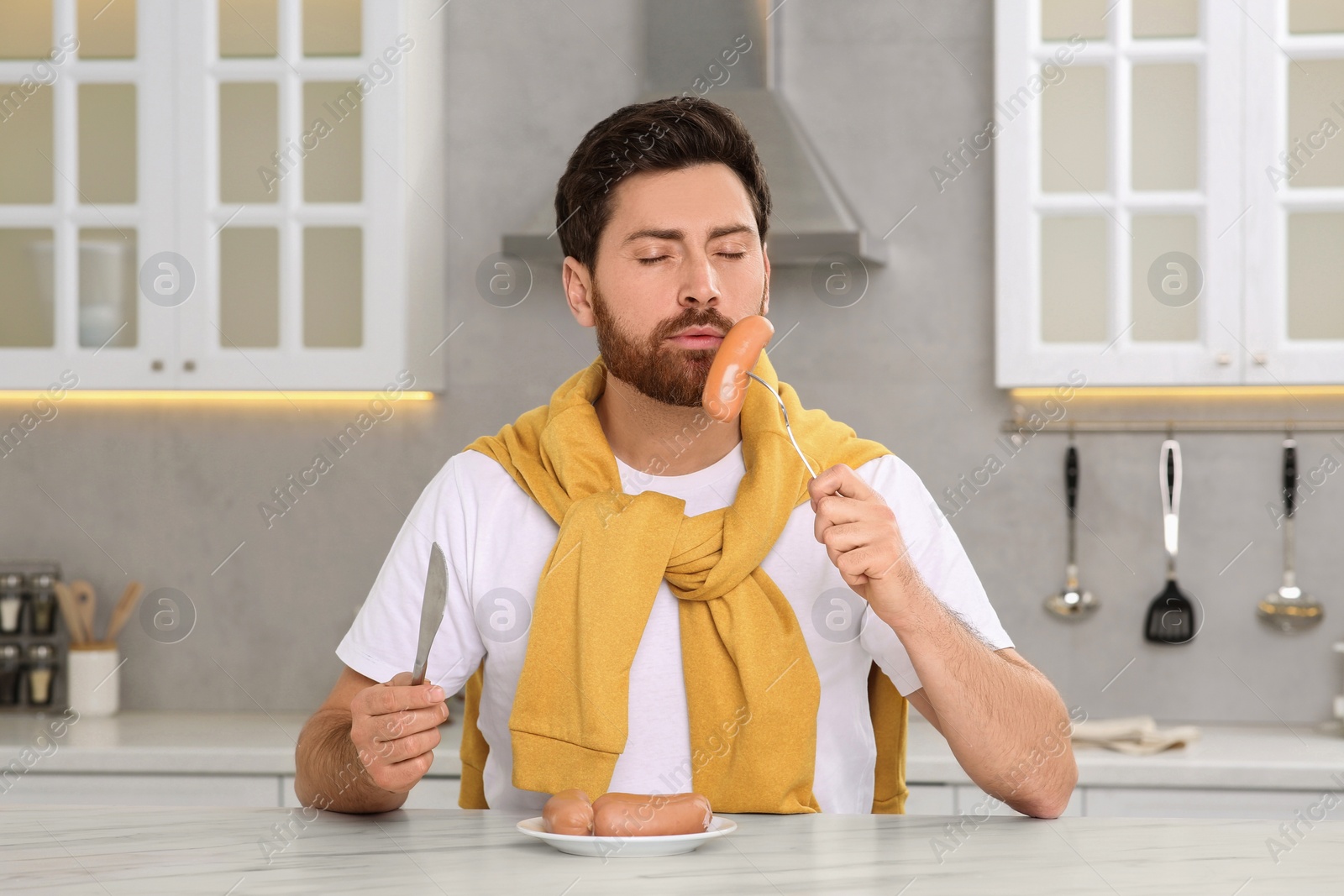 Photo of Man enjoying sausages at table in kitchen