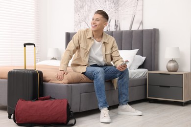 Smiling guest with smartphone on bed in stylish hotel room